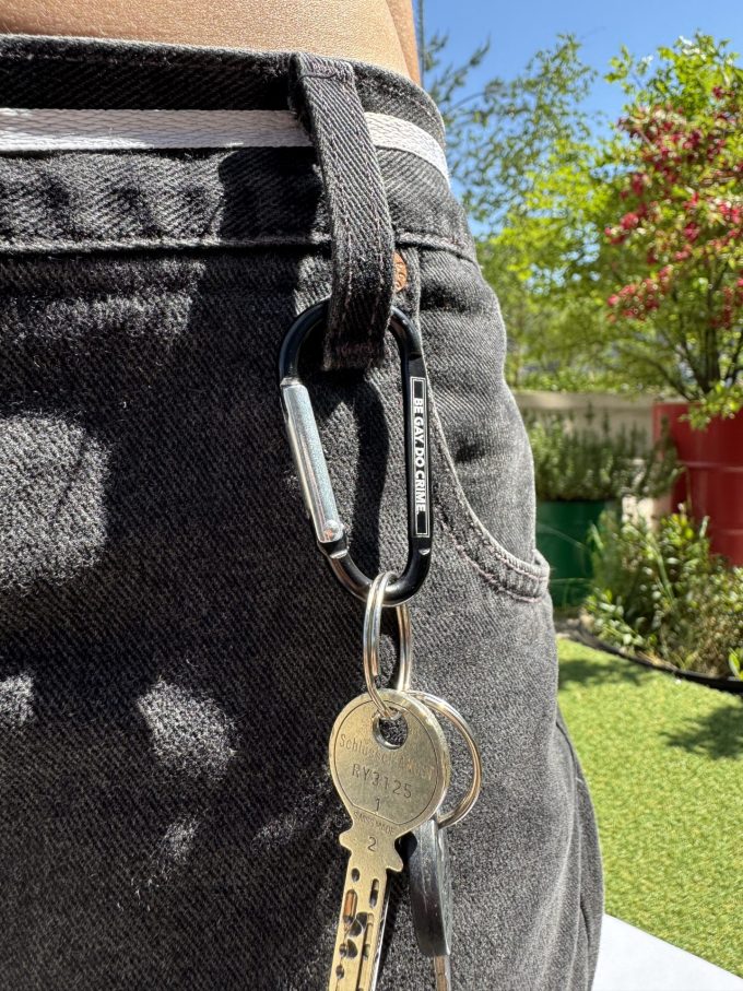 Karabiner mit Schlüsselbund am Hosenbund, Gravur «Be gay. Do crime.»