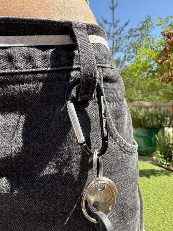 Karabiner mit Schlüsselbund am Hosenbund, Gravur «No apologies. No assimiliation.»