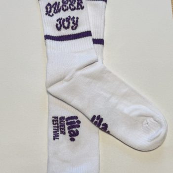 Weisse Socken mit eingestricktem Schriftzug «Queer Joy» oben und dem Logo «lia. Queer Festival» auf der Fussunterseite