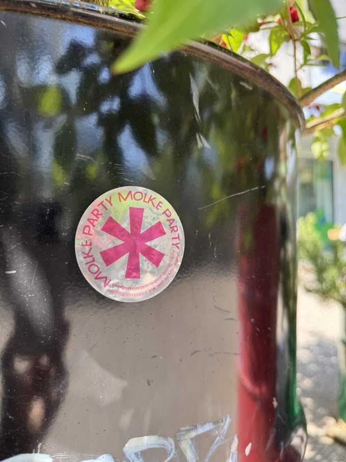 Silbriger Sticker mit pinkem Aufdruck: Grosser Genderstern und rundherum Text: «Molke Party» – Eine Welt der Milchjugend – instagram.com/milchjugend