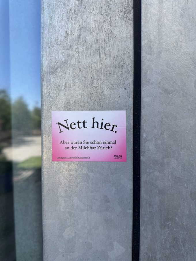 Pink-weisser Sticker mit schwarzem Text: «Nett hier. – Aber waren Sie schon einmal an der Milchbar Zürich?» –instagram.com/milchbarzuerich + Milchjugend-Logo